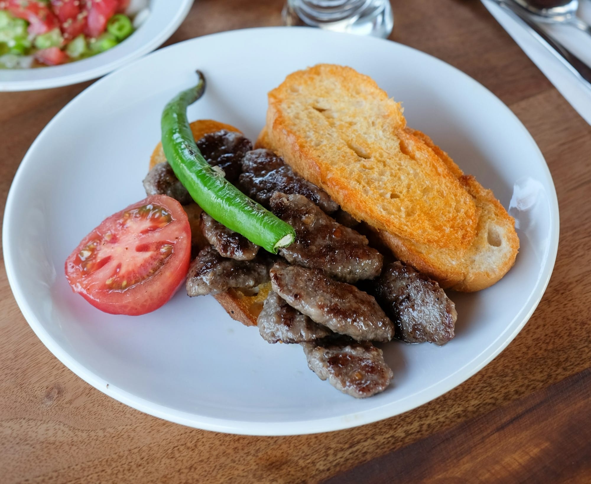 bread with meat, sliced tomato, and green chili on plate